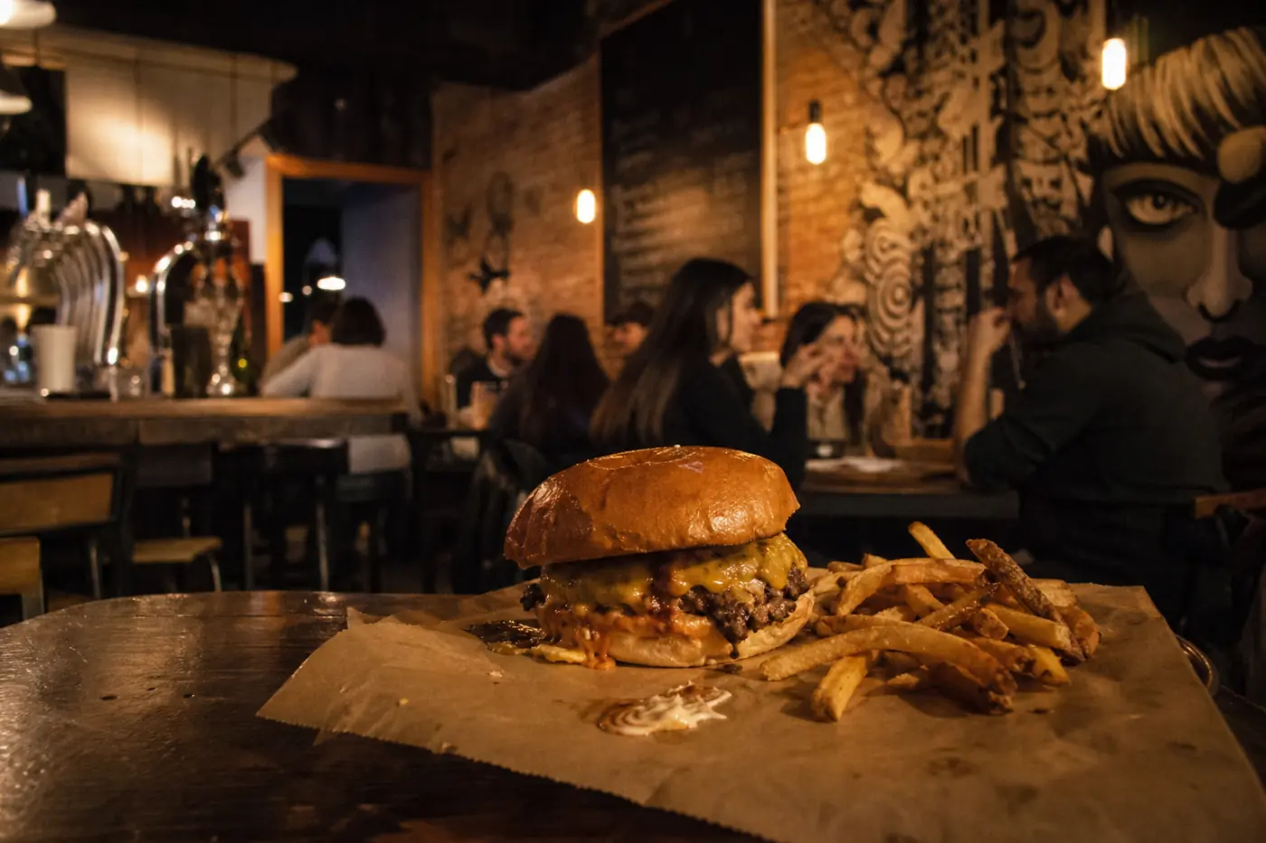 Interior del local: barra de madera con grifos de cerveza, mural en blanco y negro y bombillas cálidas